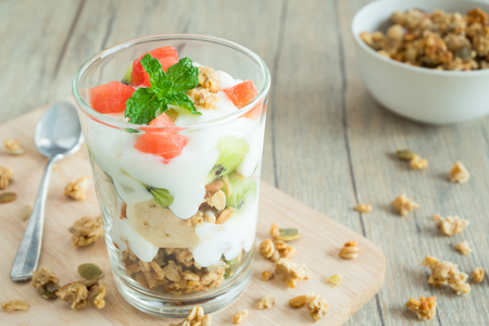 A glass of yogurt layered include garnola banana kiwi watermelon and decorated by peppermint with wood background is sprinkled by garnolaの写真素材