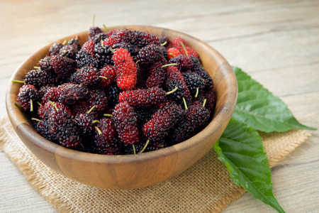 mulberry fruit in a bowl on brown mat and put leafs by the bowl with wood backgroundsの写真素材
