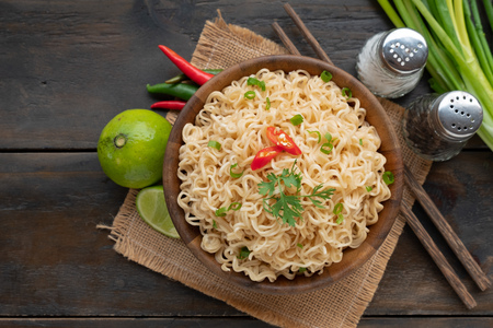 Top view instant noodle cooked menu with ingredients green onion lemon coriander and red chili feeling spicy tasty. There are put on mat and wood table and chopstick.の写真素材