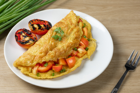 omelette tomato sliced and grill on white dish decorated with spring onion. wood table light side.の写真素材