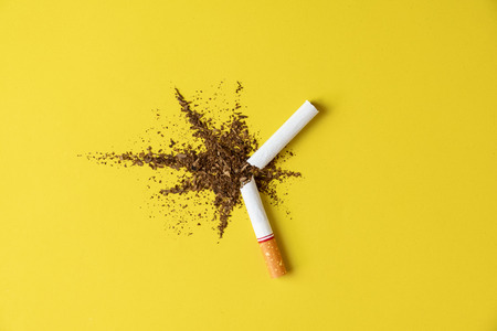 Close up cigarette broken tobacco blast spread on yellow pastel background with light side and little shadow. No and quitting smoking concept.の写真素材