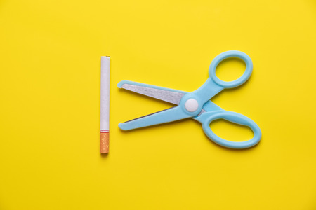 Blue scissors cut cigarette and tobacco on yellow background pastel tone. quitting smoking for teenage smoker concept.の写真素材