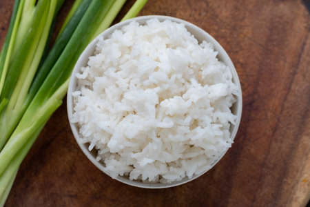 Streamed rice is asian appetizer in white bowl puton wood background  with green onions.Top view photo.の写真素材