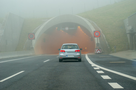 car before tunnel with speed limit signs on foggy roadの写真素材