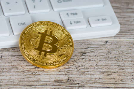 bitcoin metallic coin and white keyboard on rustic wooden tableの写真素材