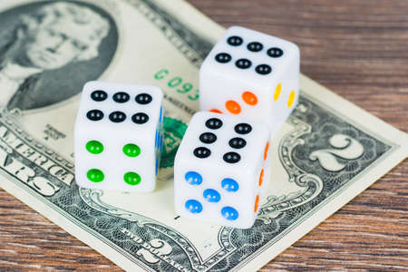 white dices with colorful dots and two dollars banknote on wooden table, last chance concept
