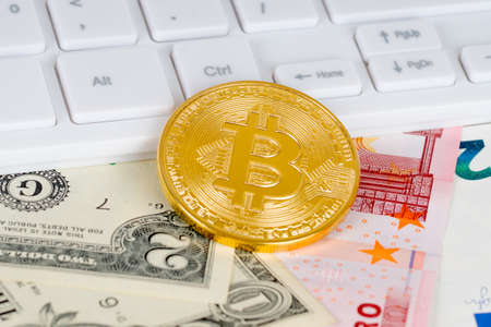 golden bitcoin metallic coin and white keyboard over dollar and euro banknotesの写真素材