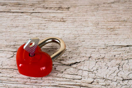 closed red heart shaped lock with key on wooden tableの写真素材