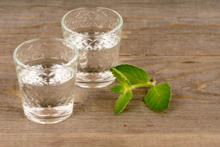 vodka with mint in shot glasses on rustic wooden tableの写真素材