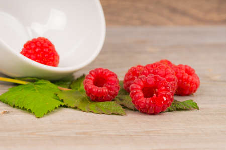 sweet juicy raspberry on green leaf, wooden table backgroundの写真素材