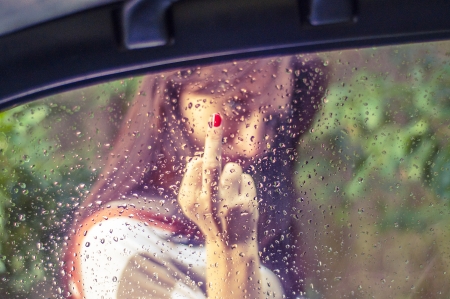 An image of girl showing her middle finger. Focus on the windowの写真素材