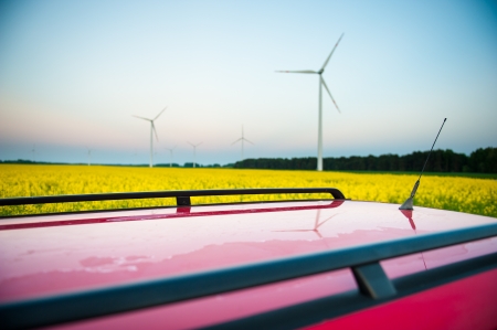 red car stands next to the field where rape flowers. and in the distance you can see the wind turbinesの写真素材