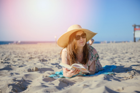 Portrait of a young brunette relaxing on the beach, reading a book. Summer timeの写真素材