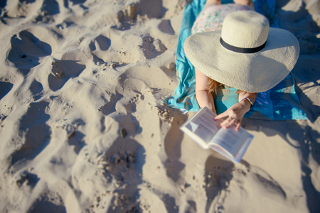 Portrait of a young brunette relaxing on the beach, reading a book. Summer timeの写真素材