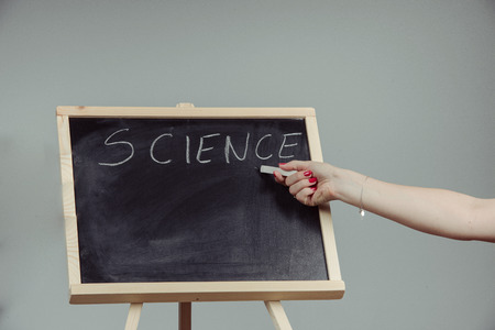 A teacher writing science, drawing chemistry elements on dark chalkboard by hand, gray backgroundの写真素材