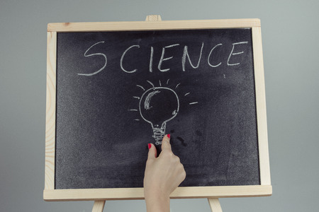 A teacher writing science, drawing chemistry elements on dark chalkboard by hand, gray backgroundの写真素材