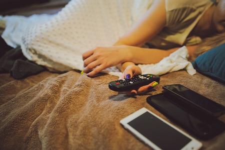 sick woman lying in bed with headache holding tv remote in handの写真素材