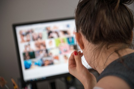 View from behind over her shoulder of a photographer editing photos on a computer with rows of images visible on the monitor.の写真素材
