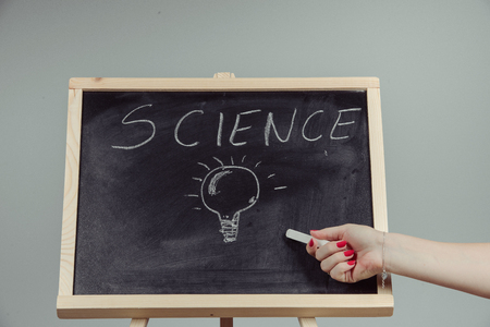 A teacher writing science, drawing chemistry elements on dark chalkboard by hand, gray backgroundの写真素材