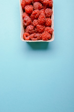 box of fresh raspberries on a blue background