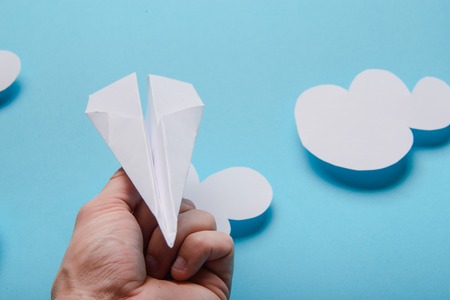 Paper plane in female hand on a blue background with cloudsの写真素材