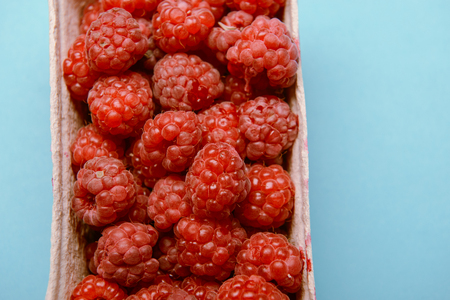 box of fresh raspberries on a blue background