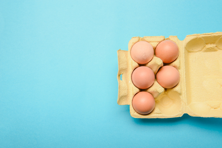 View of opened box of chicken eggs, blue background
