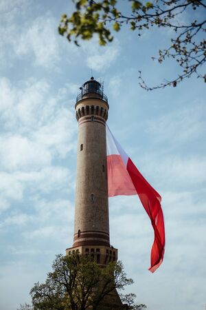Old Brick Stone Lighthouse with polish national flag. Cloudy skies. Independent Dayの写真素材
