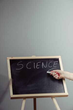 A teacher writing science, drawing chemistry elements on dark chalkboard by hand, gray background