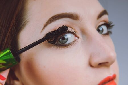 Young and beautiful woman paints eyelashes, Close up look at the face