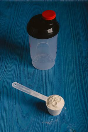 protein supplement powder in plastic spoon on blue wooden backgroundの写真素材
