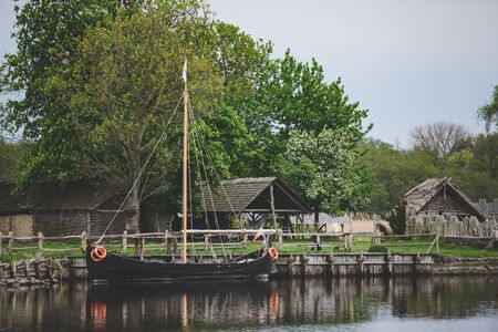 Old wooden viking huts in a village with ship moored at the bank.