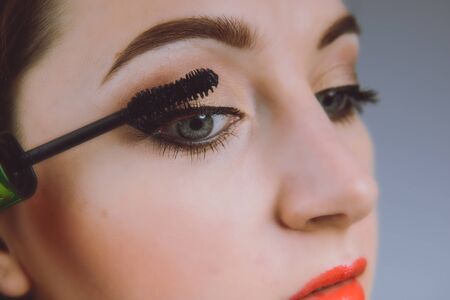 Beauty model teenage girl looking in the mirror and applying mascara make up. Beautiful young woman apply makeupの写真素材