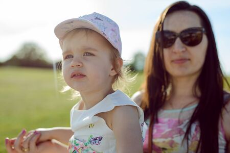 Happy mother and daughter in the park. Beauty nature scene with family outdoor lifestyle. Happy family resting together on the green grass, having fun outdoor. Happiness and harmony in family life.の写真素材