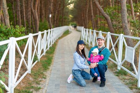 Happy mother, father and daughter in the park. Beauty nature scene with family outdoor lifestyle. Happy family resting together on the green grass, having fun outdoor. Happiness and harmony in family life.の写真素材