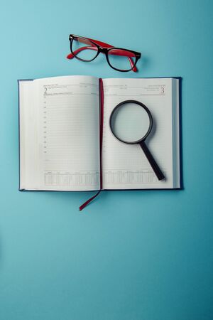 Business planning with copy space and office supplies. Magnifying glasses and red glasses on blue backgroundの写真素材