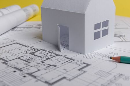 White family paper house, house projects plan and blueprints on yellow background paper. Minimalistic and simple concept, style. Horizontal orientationの写真素材