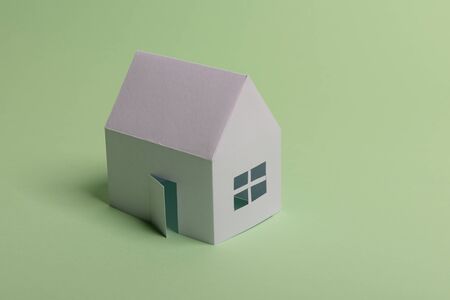 White family paper house in man hand on mint background paper. Minimalistic and simple concept, style. Copy space. Horizontal orientationの写真素材