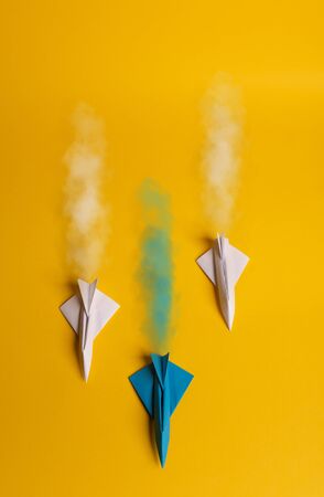 Group of paper plane in one direction and with one individual pointing in the different way on yellow background. Smoke coming out from aircraft tailsの写真素材
