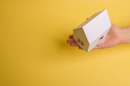 White family paper house in man hand on yellow background paper. Minimalistic style. Copy space. View from above. Horizontal orientationの写真素材