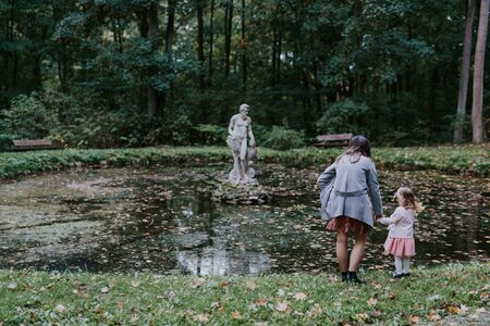 Beautiful little looking at the statue in the pond. Sunny day. Autumn dayの写真素材
