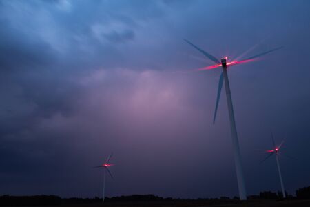 Wind turbines on a dramatic dark blue clouds in the sky. Storm ahead is coming. Red warning light on...