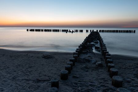 A photograph of wooden breakwater and seagulls at sunset on the Baltic Seaの写真素材