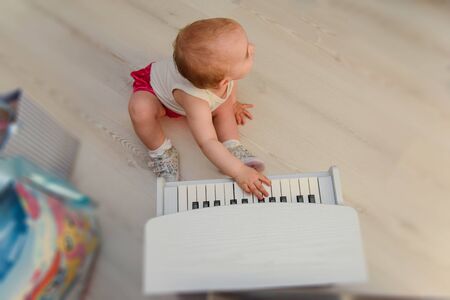 beautiful baby girl playing toy piano in light room. Authentic image.の写真素材