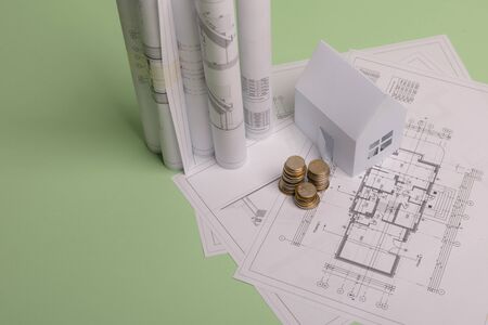 White family paper house , stack of money coins, house projects plan and blueprints on mint background paper. Minimalistic and simple concept, style. Vertical orientationの写真素材