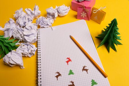 gift box and green paper origami trees with notepad on yellow desk, table. Christmas to do list text.の写真素材