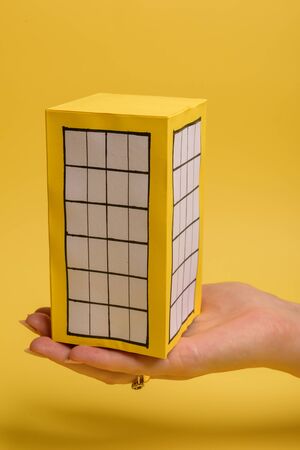 White family paper house over block of flats on yellow background paper. Minimalistic and simple concept, style. Copy space. Vertical orientation.の写真素材