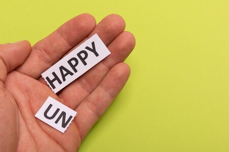 man hand holding card with text unhappy, cutting word 'un' so it written 'happy'. Copy space. Lime background. Studio shoot.の写真素材