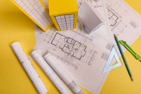 White family paper house, house projects plan and blueprints in the background. Minimalistic and simple concept, style. Horizontal orientation. View from above.の写真素材