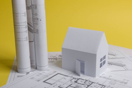 White family paper house, house projects plan and blueprints in the background. Minimalistic and...